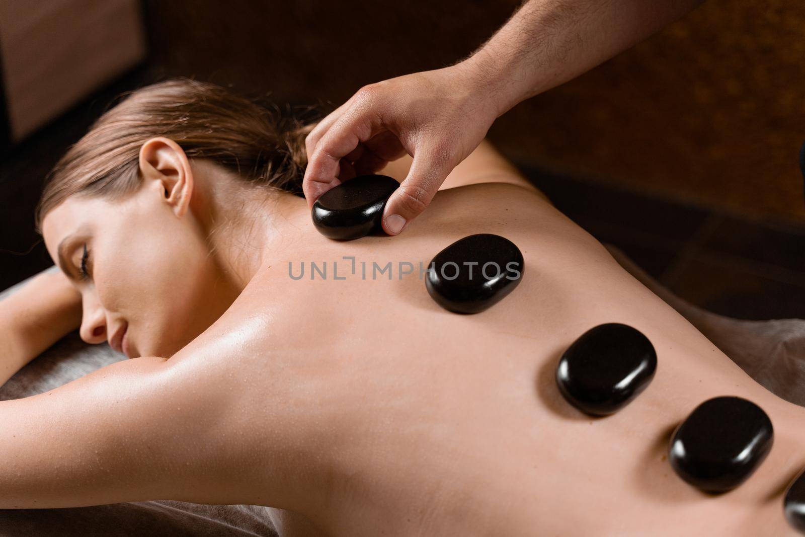 Masseur placed hot stone on the back of woman. Manual therapy in spa