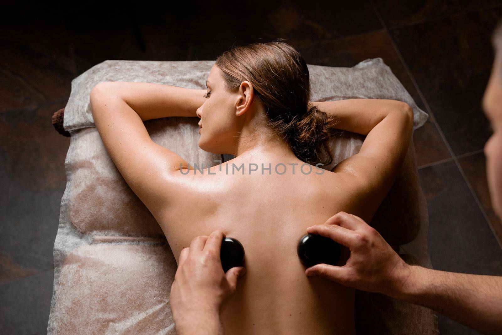 Hot stone massage therapy for relax and ease tense muscles and damaged soft tissues of body. Heated stones are placed on specific parts young woman.