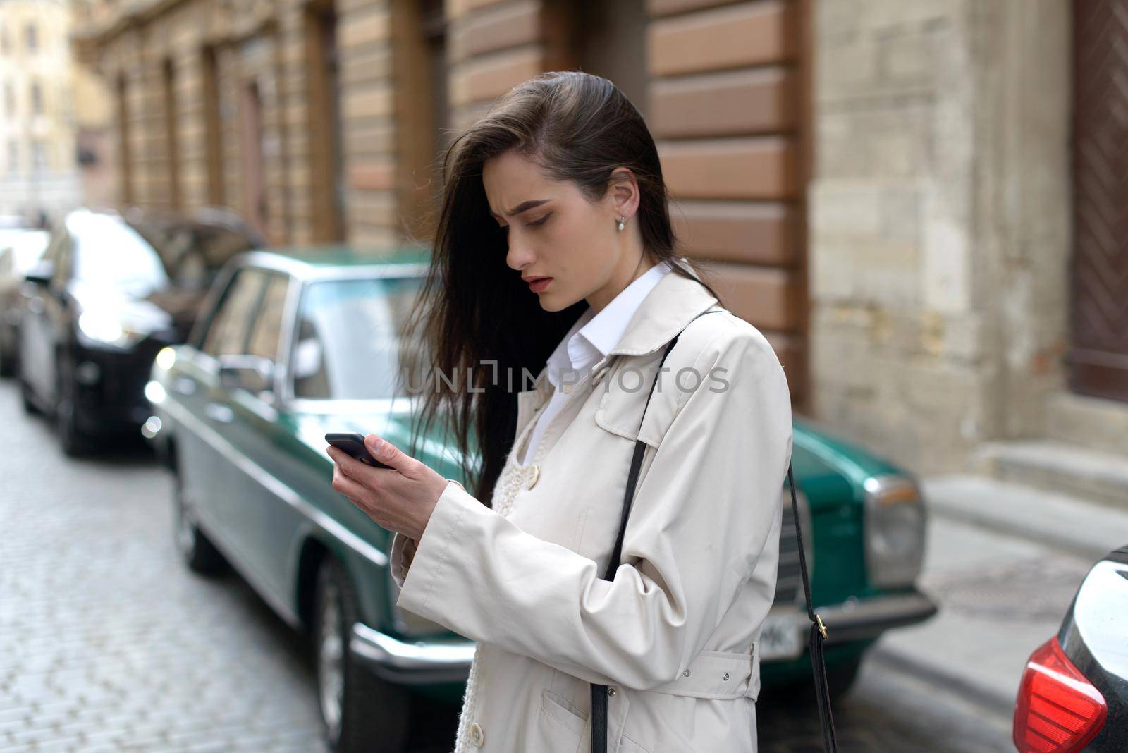 A woman on the street uses a mobile phone. online shopping. use of mobile applications. beautiful woman with long dark hair in a raincoat