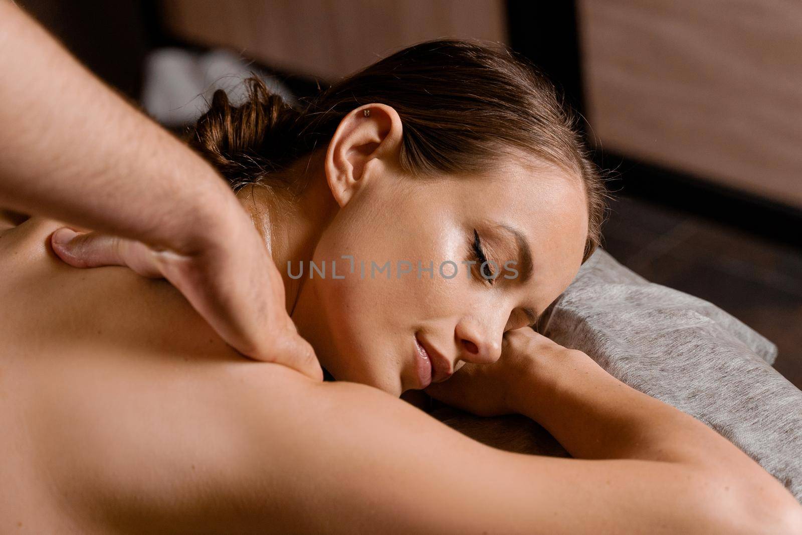 Attractive girl is relaxing on classic massage procedure in spa. Manual therapy. Masseur is doing shoulder massage