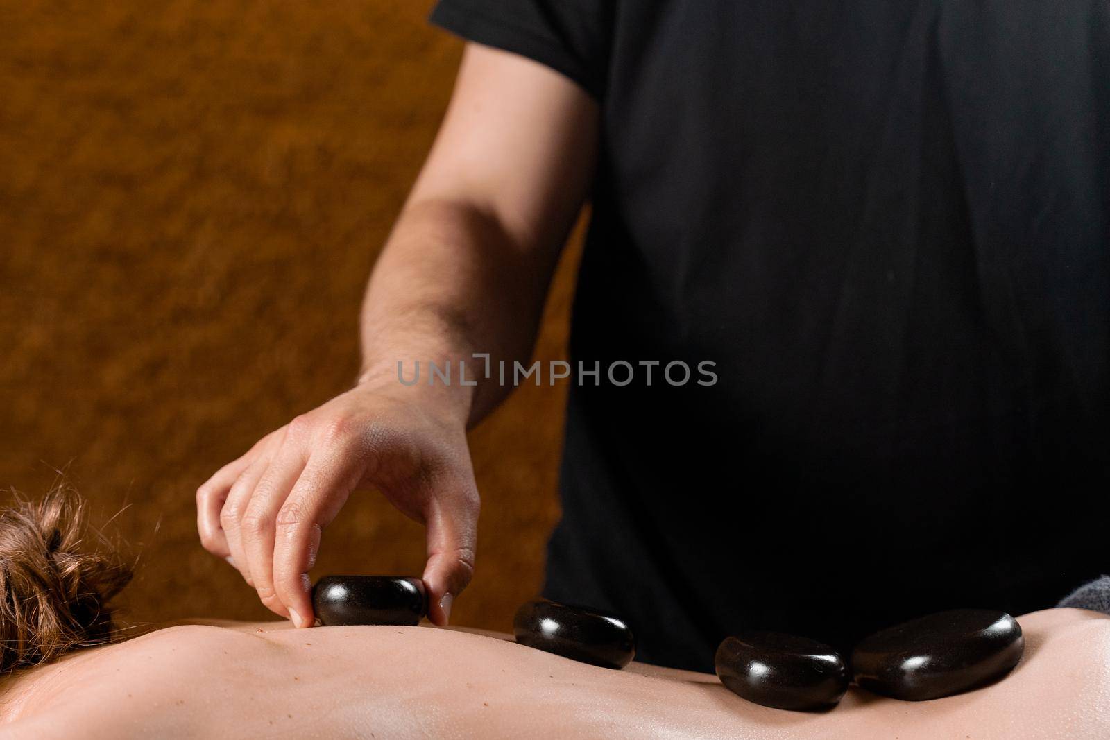 Heated stones on back of woman. Stone massage therapy in spa for relaxing