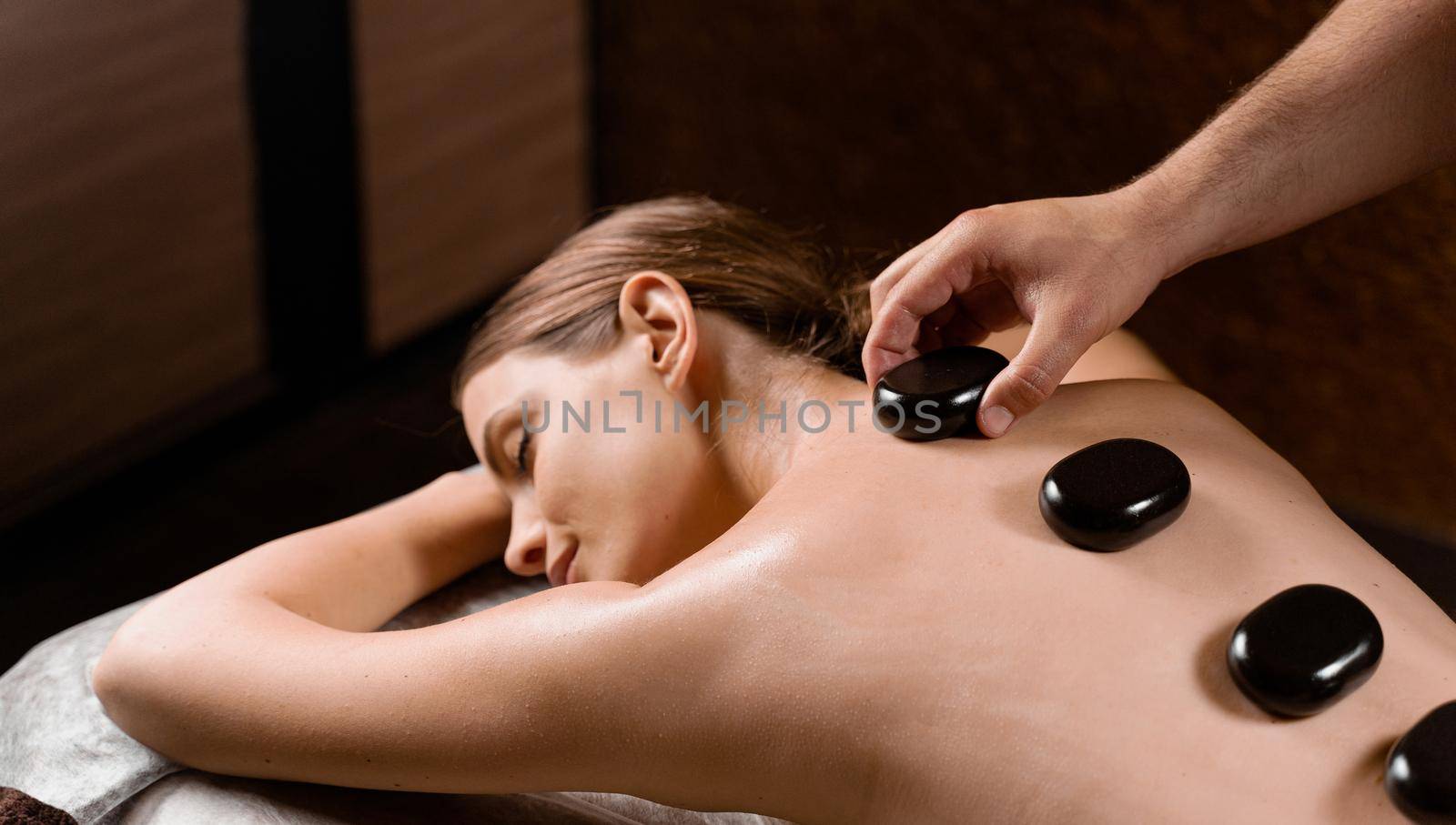 Masseur placed hot stone on the back of woman. Manual therapy in spa. by Rabizo