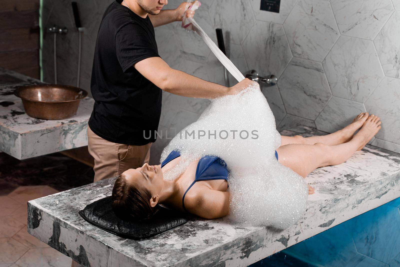 Foam peeling in spa. Woman is laying on back and relaxing. Turkish hammam procedure