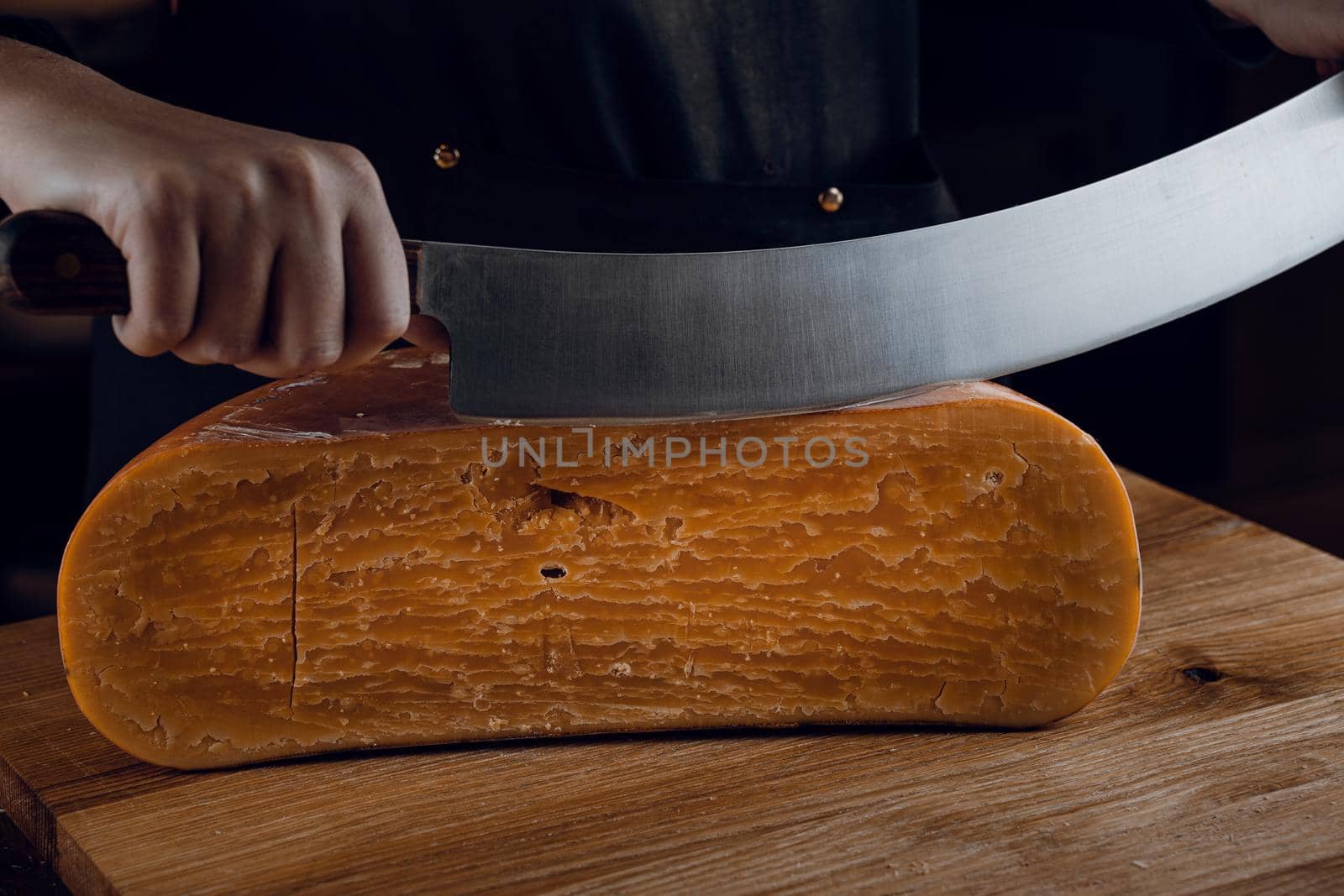 Slicing aged cheese parmesan with crystals using a cheesy dutch knife. Hard cheese with knife on dark background