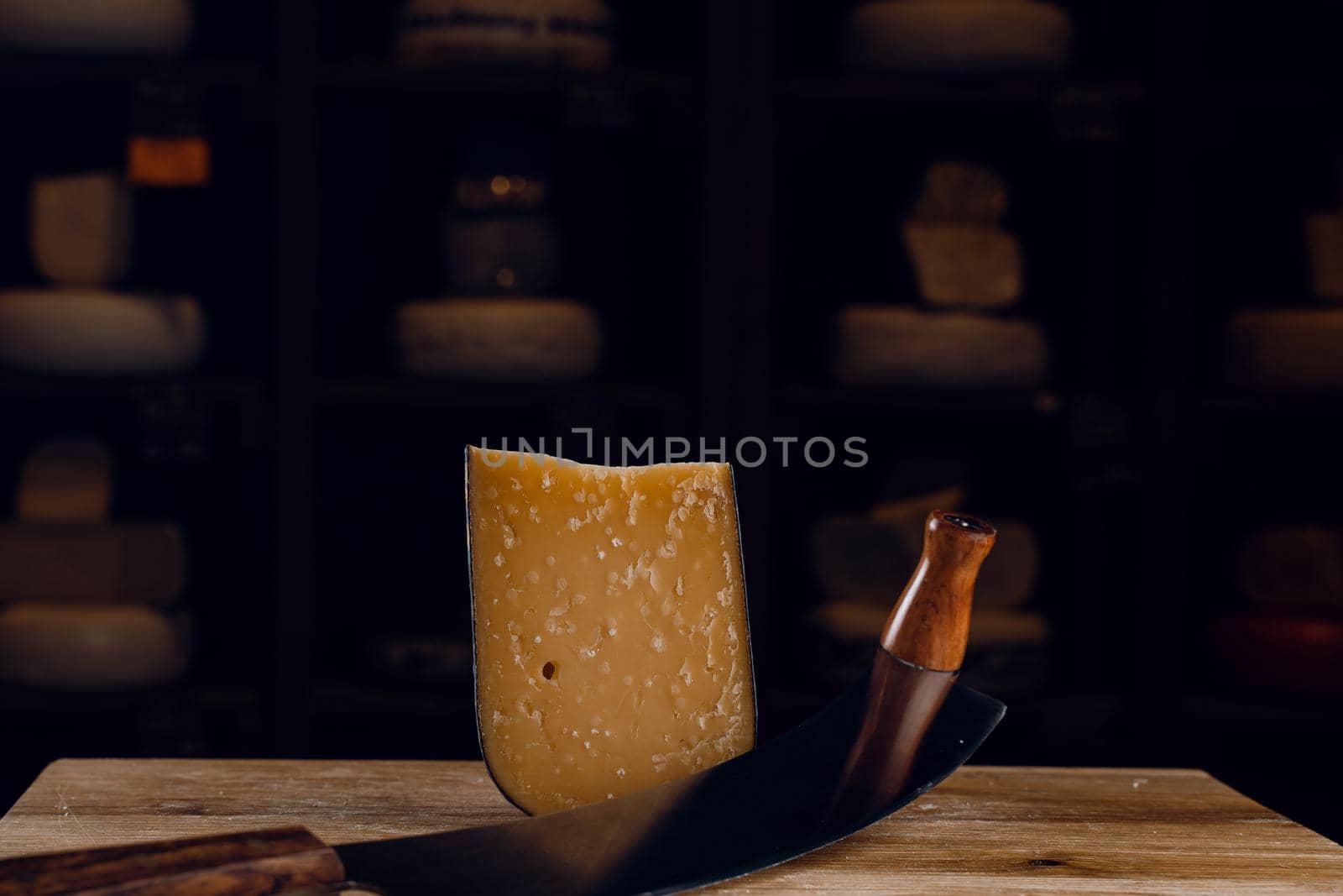 Parmesan hard aged cheese with dutch cheese knife on dark background. Snack tasty piece of cheese for appetizer. by Rabizo
