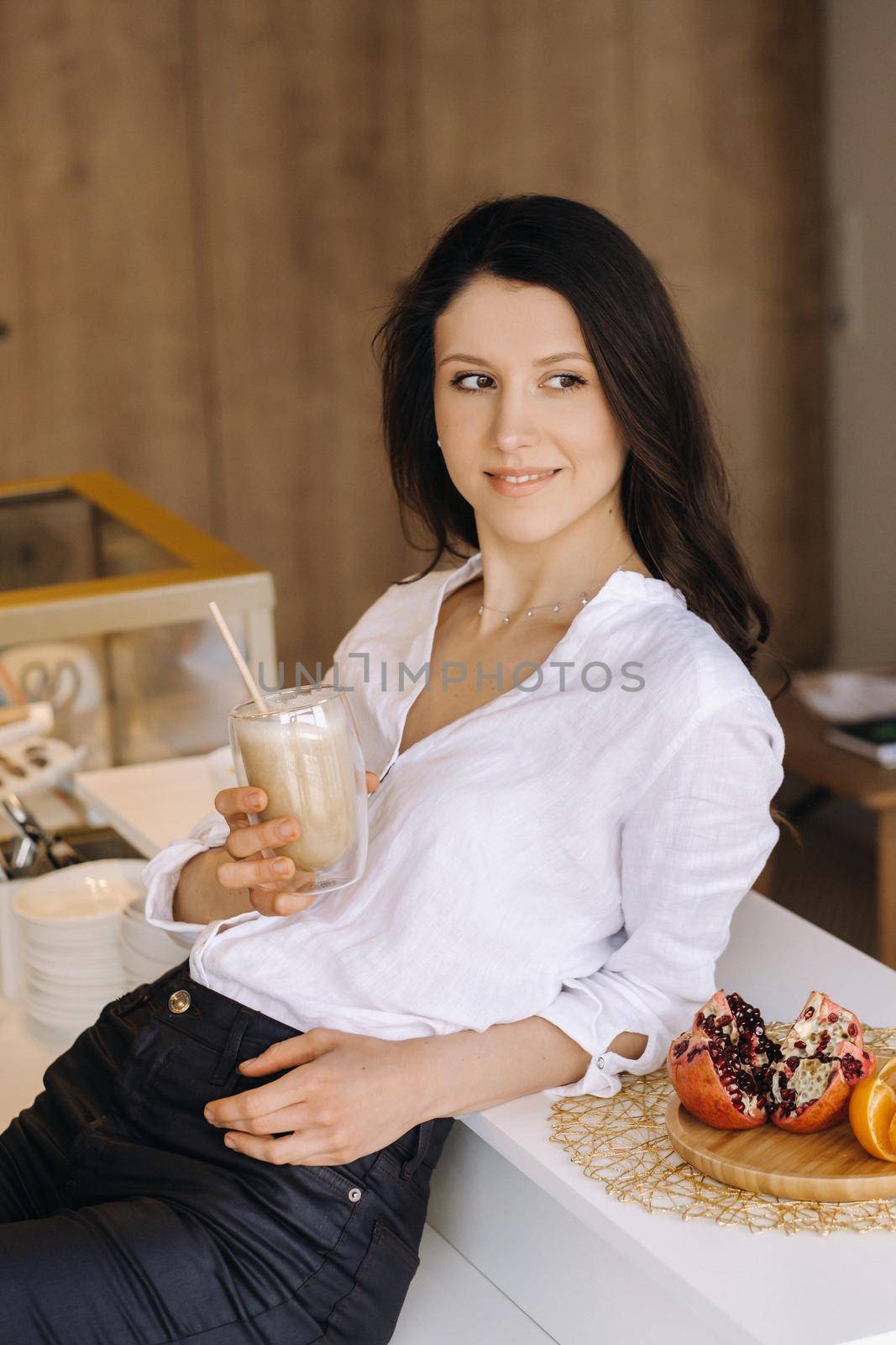 A happy healthy woman is holding a fruit cocktail in her hands, standing at home in the kitchen.Healthy eating.