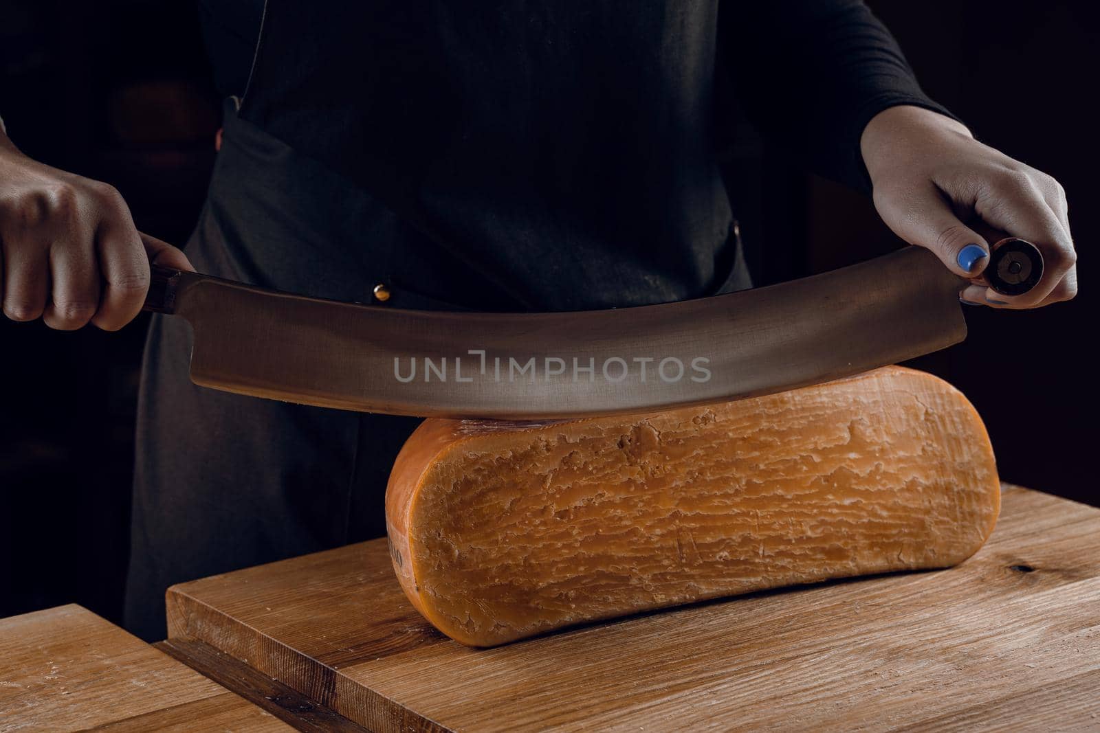 Slicing aged cheese parmesan with crystals using a cheesy dutch knife. Hard cheese with knife on dark background. by Rabizo