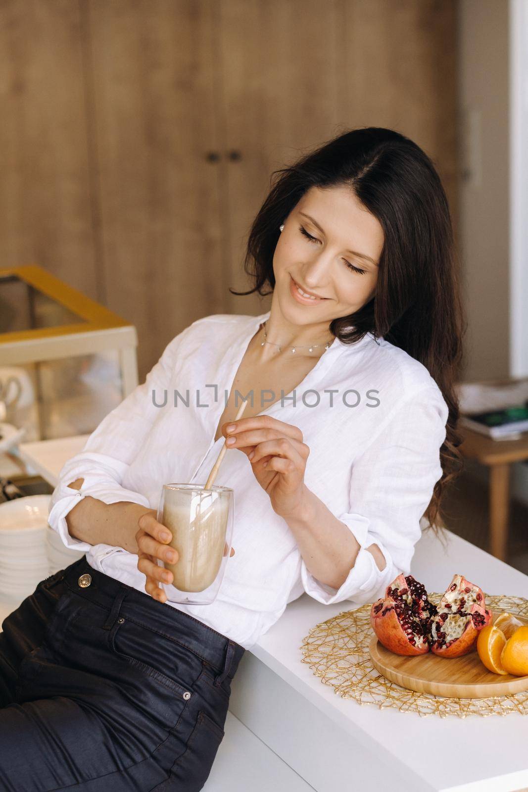 A happy healthy woman is holding a fruit cocktail in her hands, standing at home in the kitchen.Healthy eating.