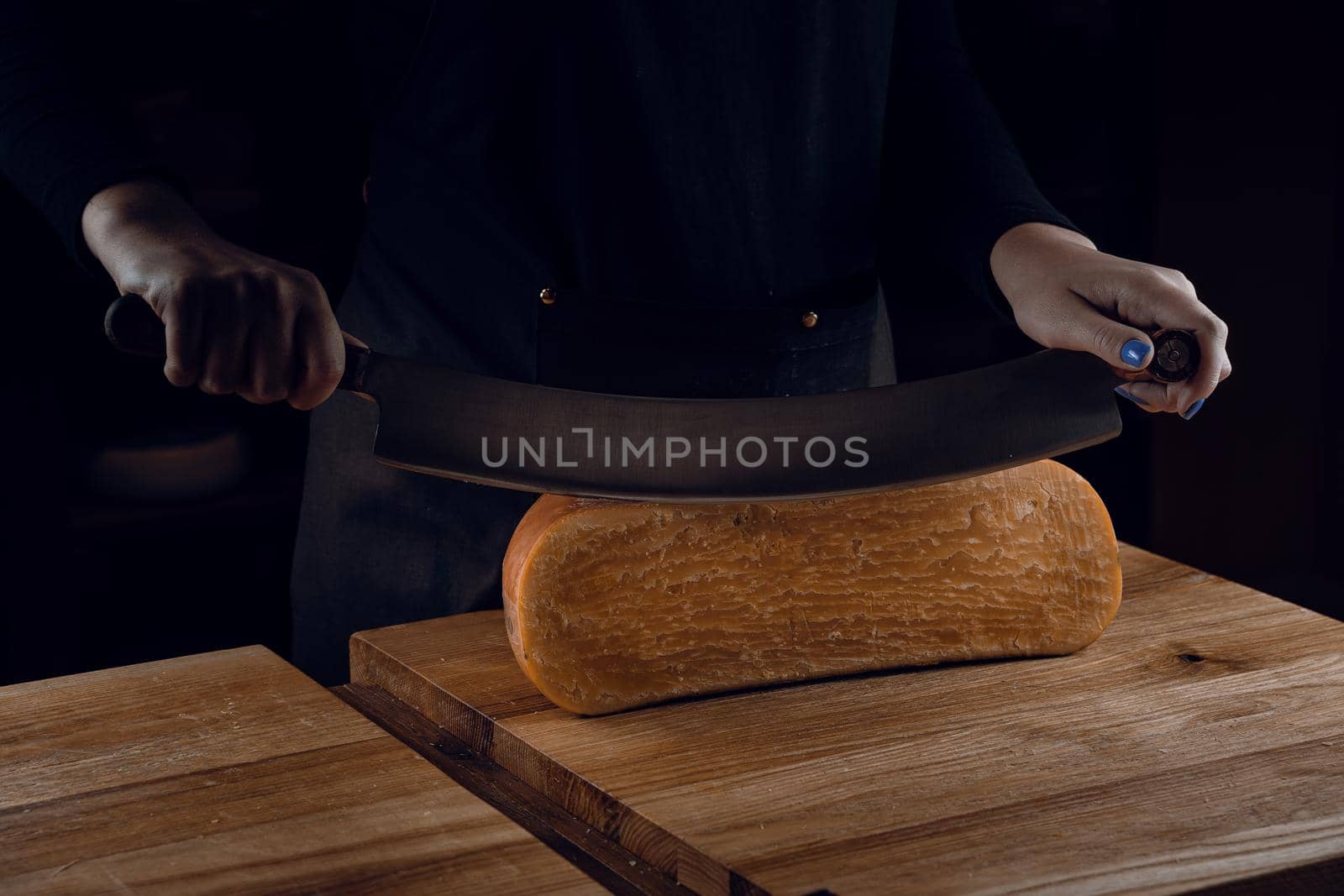 Slicing aged cheese parmesan with crystals using a cheesy dutch knife. Hard cheese with knife on dark background