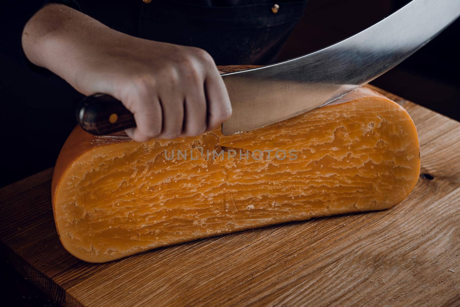 Slicing aged cheese parmesan with crystals using a cheesy dutch knife. Hard cheese with knife on dark background