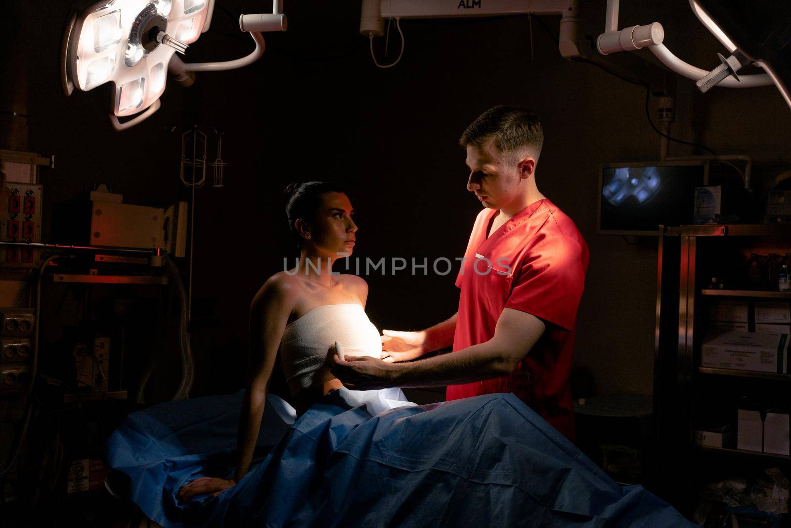 Surgeon with woman patient in operating room before breast augmentation for girl. Doctor wraps around the patient chest after breast augmentation.