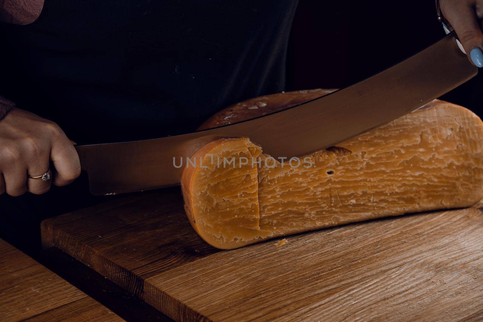 Slicing aged cheese parmesan with crystals using a cheesy dutch knife. Hard cheese with knife on dark background