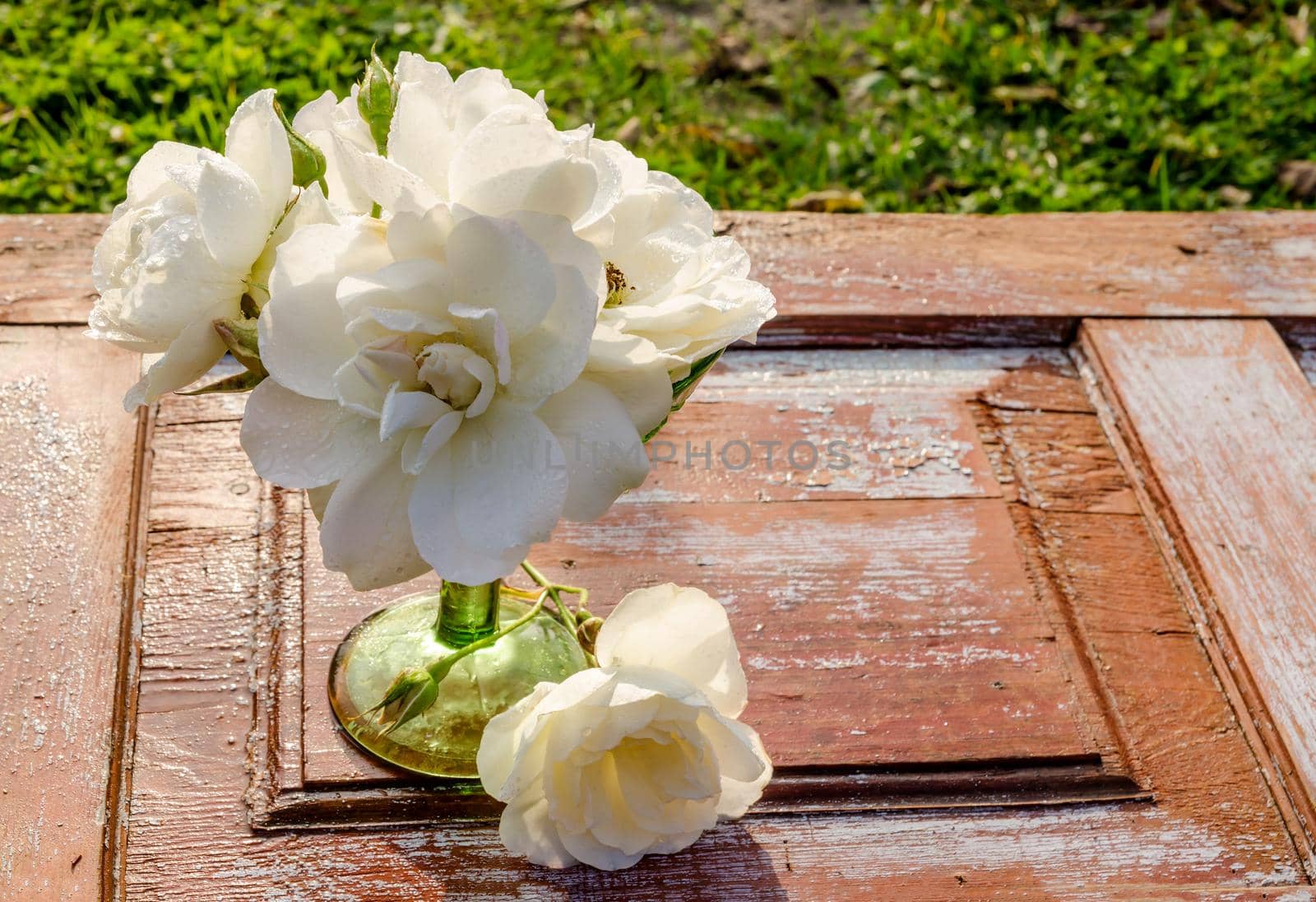 Beautiful bouquet of roses with drops in green glass vase on old wooden table by zimages