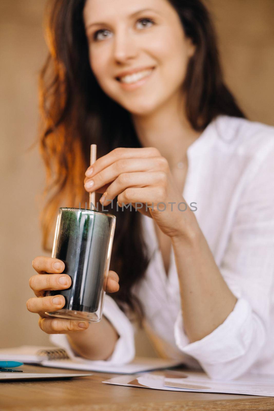 A young freelance woman with a cocktail in her hands at her workplace at work by Lobachad