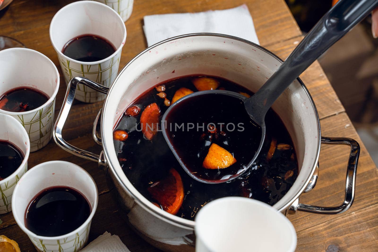 Red mulled hot and spiced wine alcohol drink pouring into disposabla glass. Grog with cinnamon seasonal christmas drink