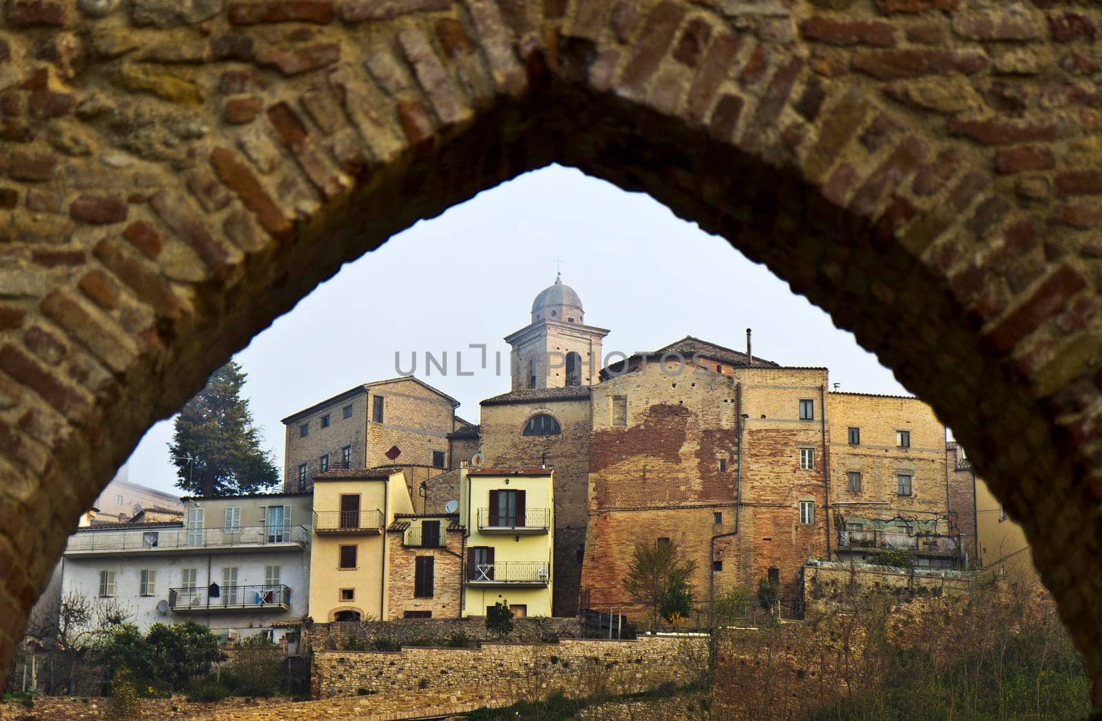 The buildings of Ripatransone in the Marche region of Italy are seen through a stone arch