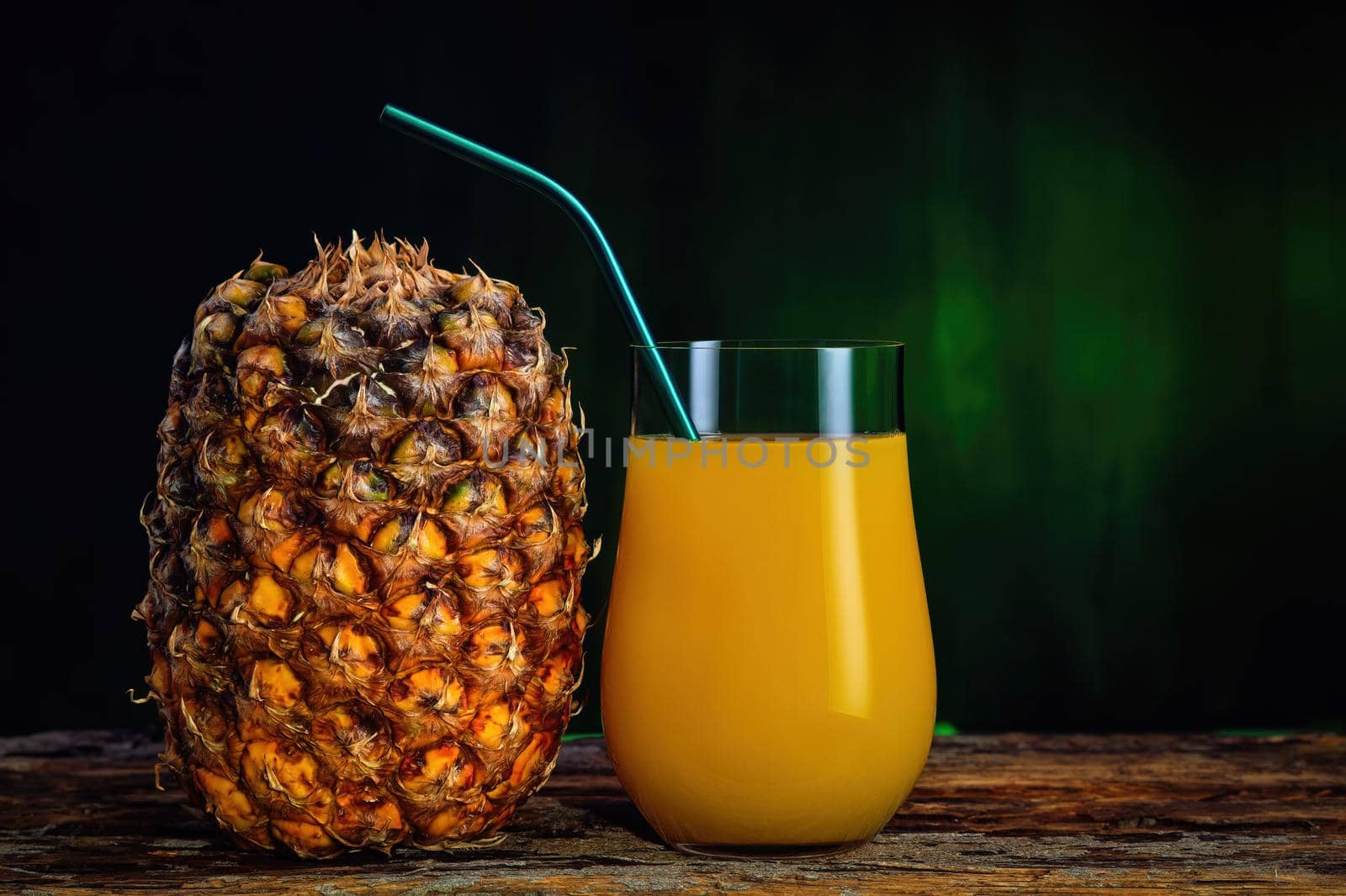 Fresh pineapple juice in a glass and fresh pineapple on a dark green background by Fischeron