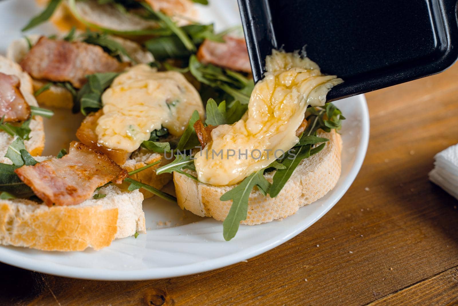 Raclette melted cheese for sandwich with fried bacon and arugula traditional french cuisine. Plate with snacks