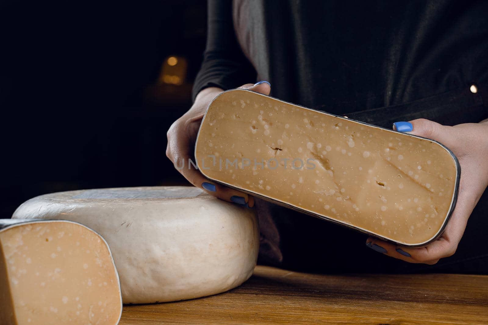 Holding goat cheese wheel and big pieces of it. Mix of cheeses from goat milk.