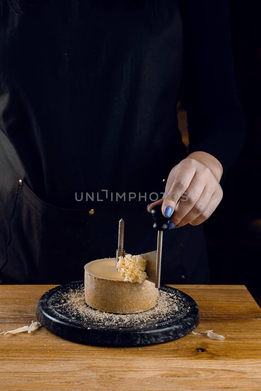 Shaving tete de moine cheese using girolle knife. Monks head. Variety of Swiss semi-hard cheese made from cows milk by Rabizo