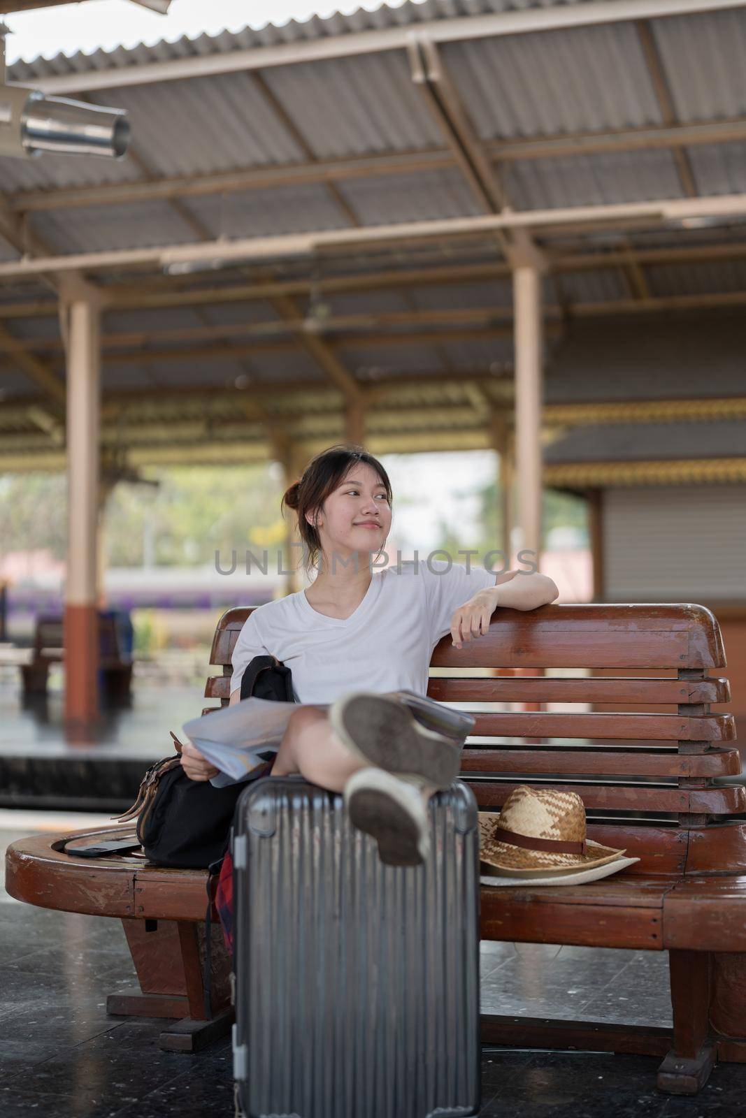 Happy young asian woman traveler or backpacker using map choose where to travel with luggage at train station, summer vacation travel concept.