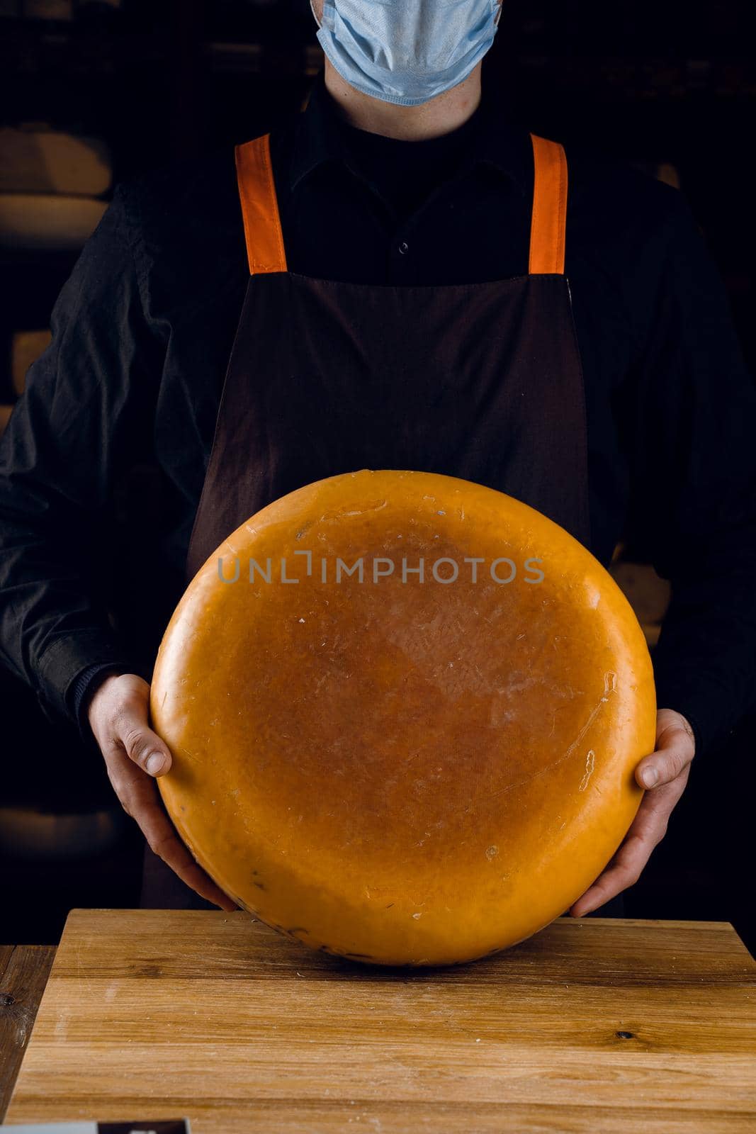 Big yellow cheese wheel in hands. Seller in mask for protection against coronavirus covid-19. holding round cheese