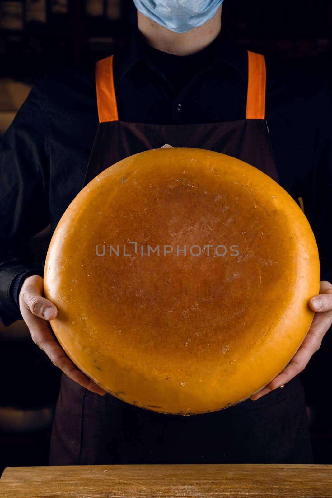 Big yellow cheese wheel in hands. Seller in mask for protection against coronavirus covid-19. holding round cheese