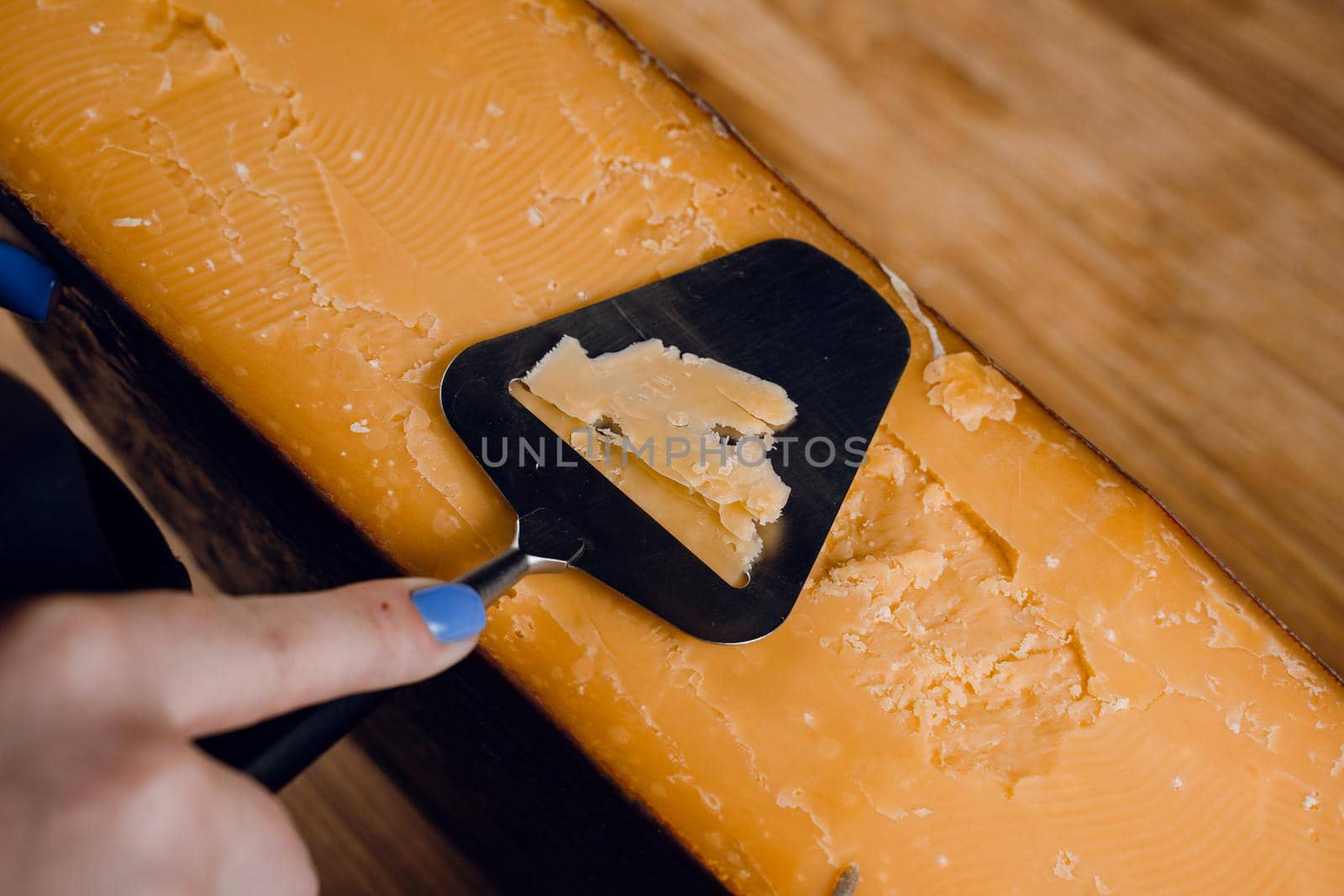 Slicing aged cheese parmesan with crystals using slicer knife. Hard cheese with knife for appetizer on dark background