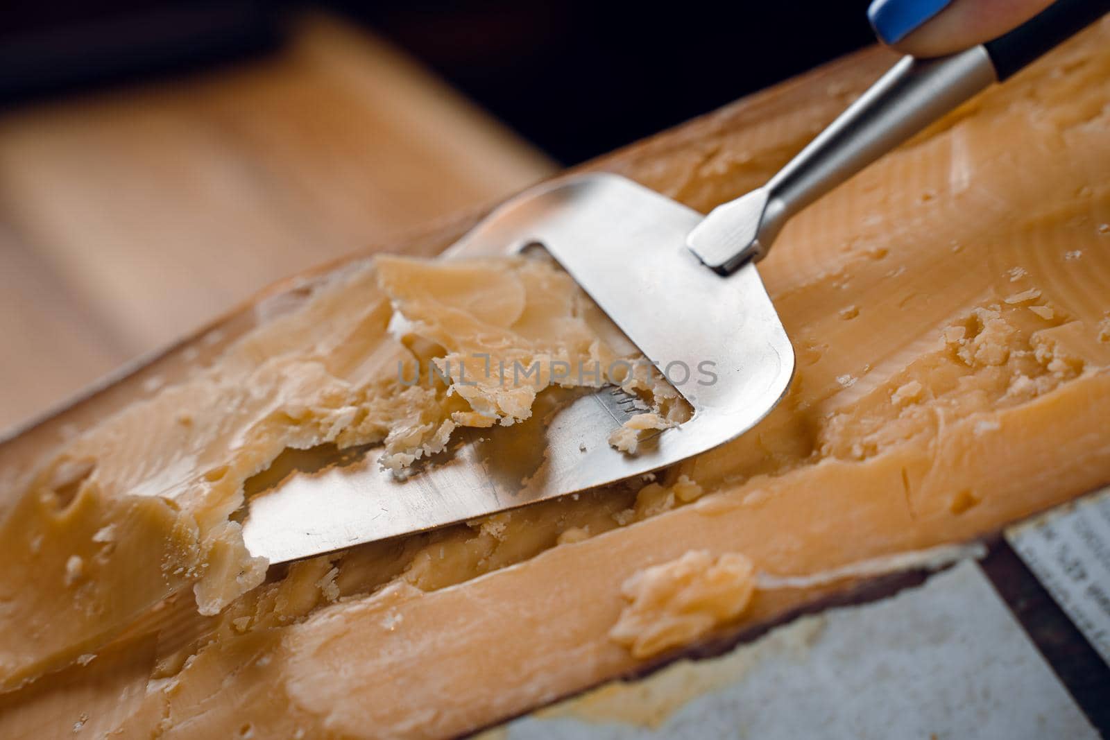 Slicing aged cheese parmesan with crystals using slicer knife. Hard cheese with knife for appetizer on dark background