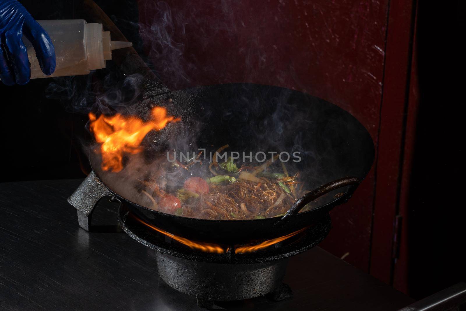 Funchoza flambe rice noodles with vegetables cooking on fire in wok pan. Street food