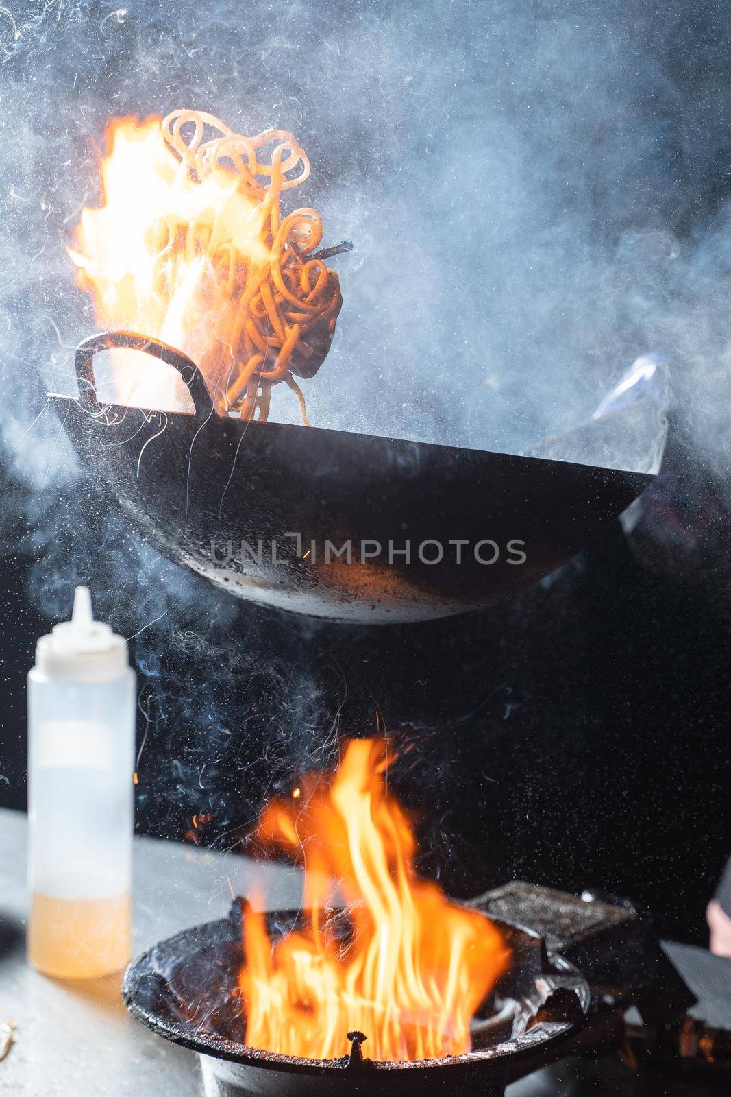 Flying flambe noodles for wok box with meat, soy sauce fried in a wok pan, street food.