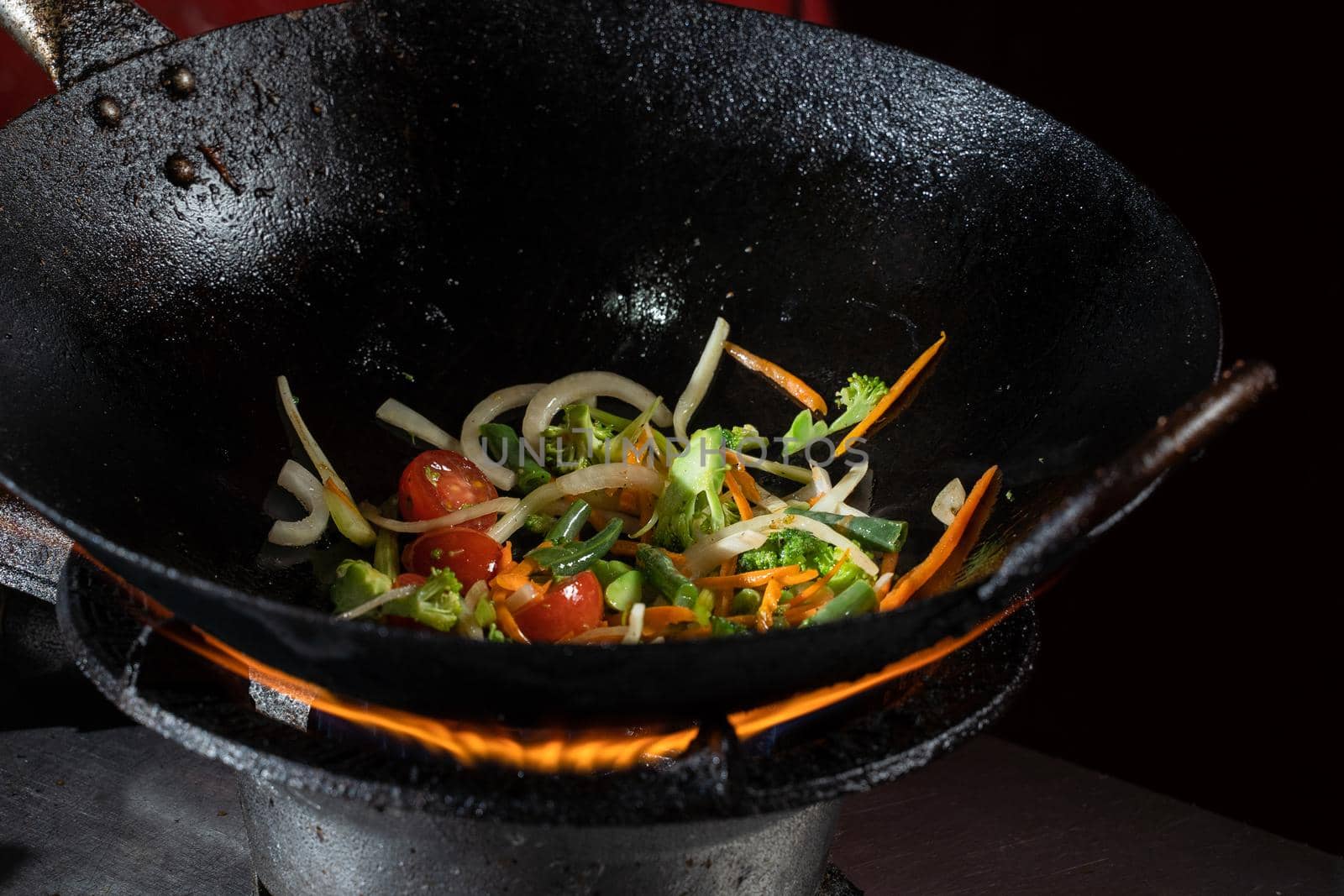 Frying vegetables in a wok pan onions, broccoli, tomatoes cherry, carrot, asparagus.