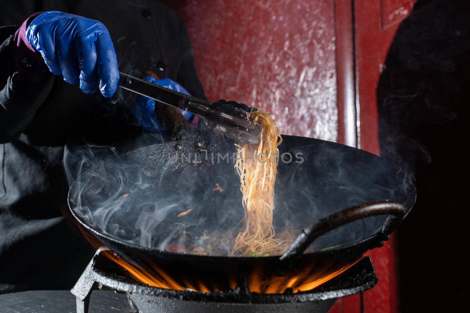 Funchoza rice noodles with vegetables cooking on fire in wok pan. Street flambe food.