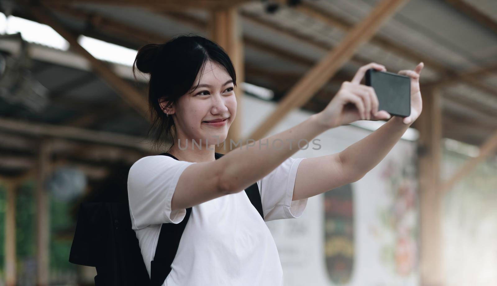 Tourist woman aling selfie with a smartphone while at the train station. Enjoying travel concept. Girl using smartphone while at the railway station platform..