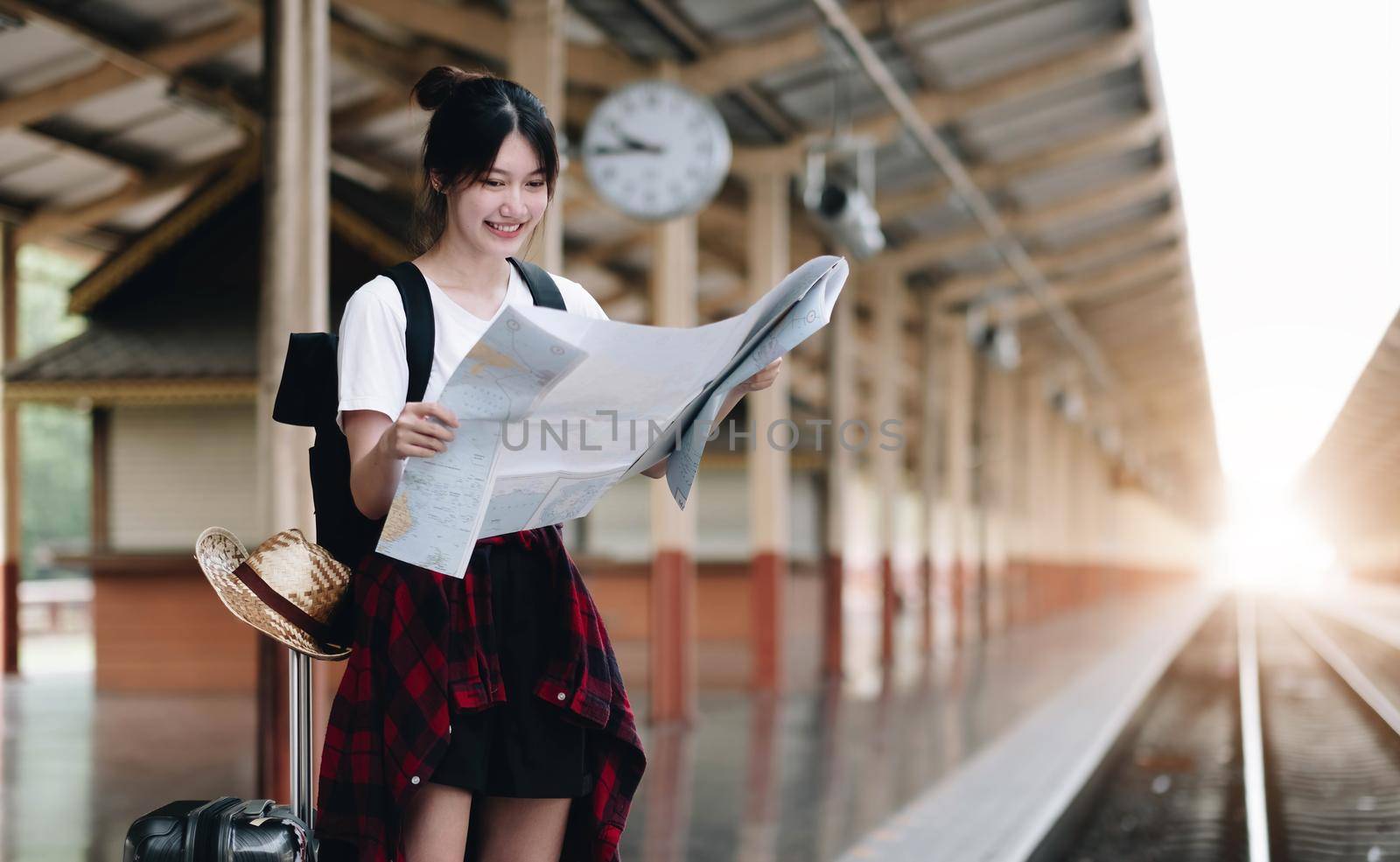 Young woman traveler with luggage and hat looking at map with train background at train station. travel concept