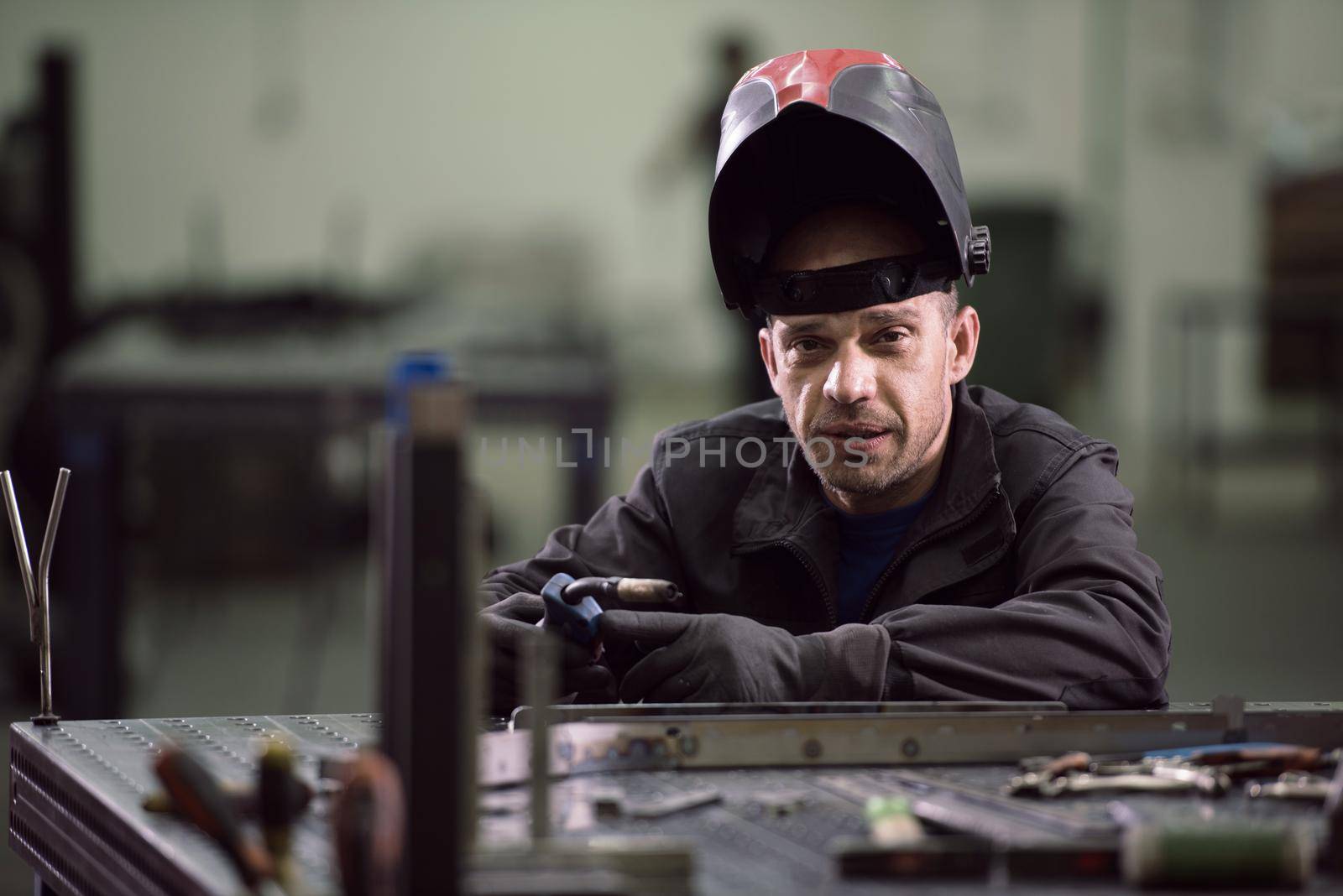 Portrait of Young Professional Heavy Industry Engineer. Worker Wearing Safety Vest and Hardhat Smiling on Camera. In the Background Unfocused Large Industrial Factory . High quality photo