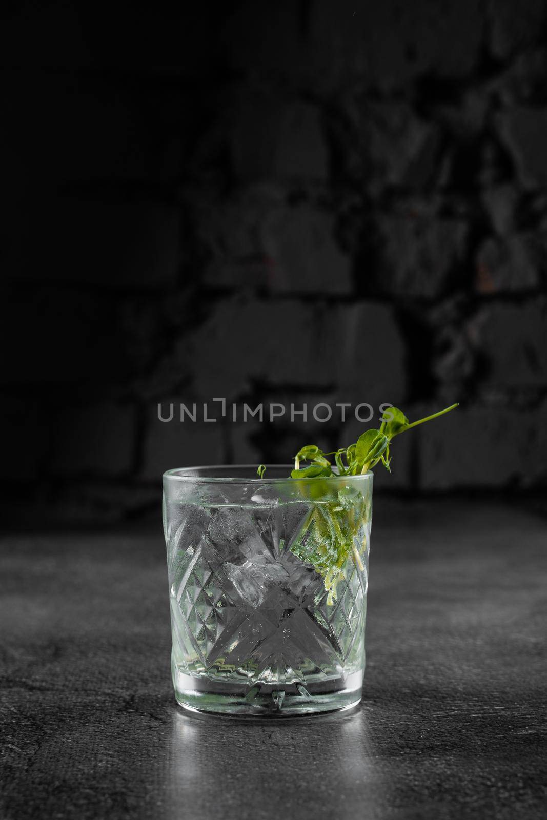 Glass with drink, ice on gray background. Alcohol cocktail decorated microgreen