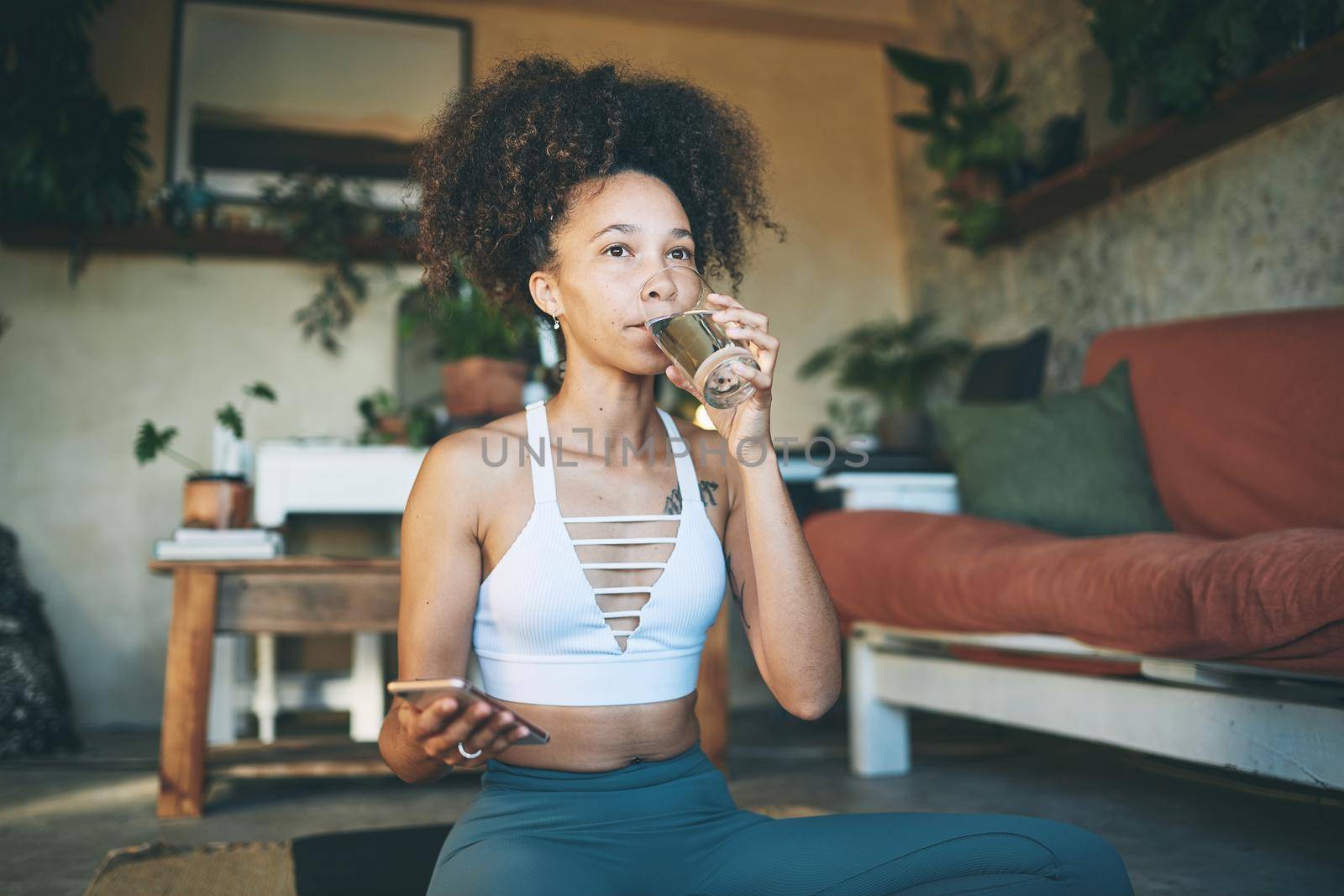 Shot of a young beautiful girl in her sportswear browsing on her smartphone and drinking a glass of water