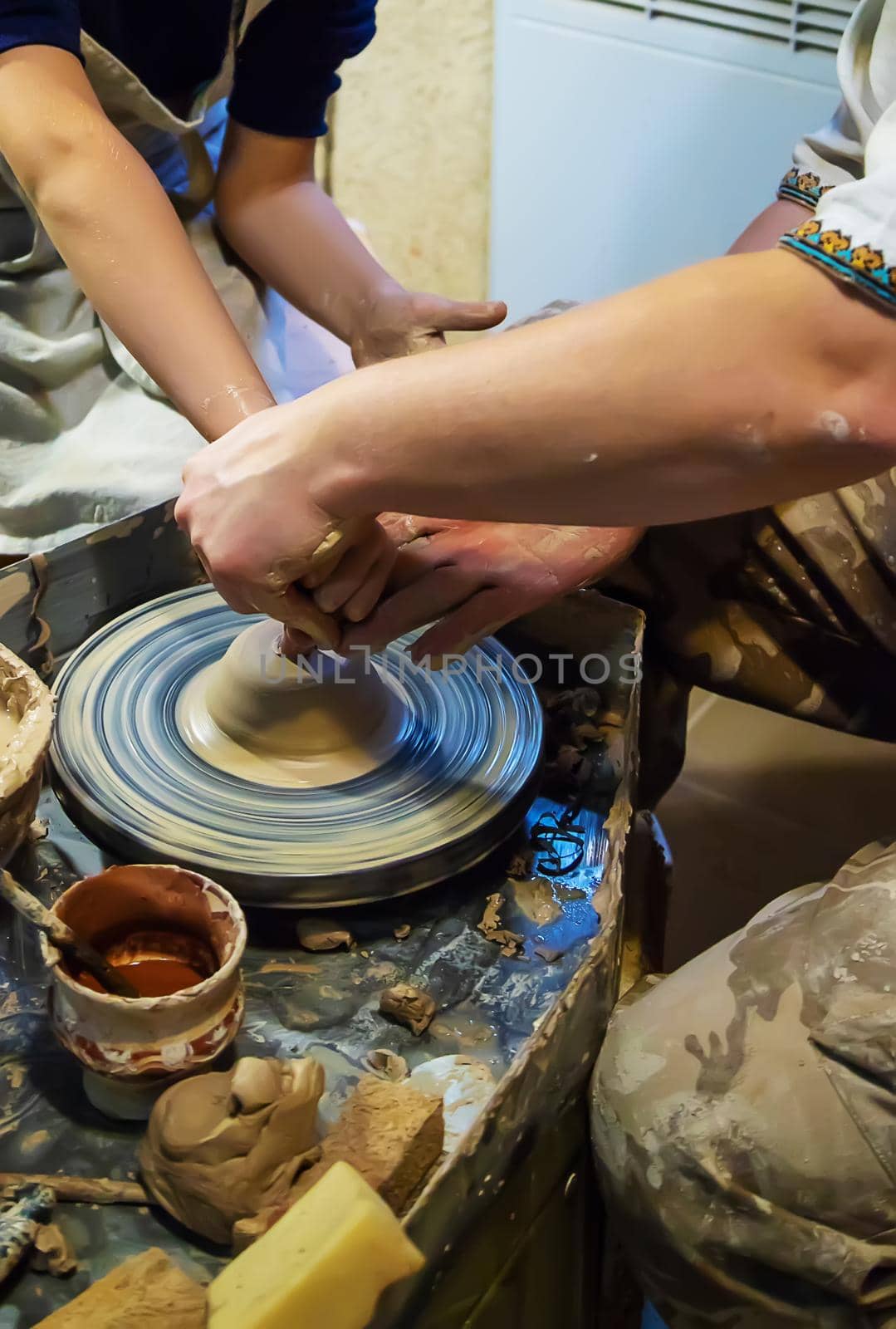 the Hands of a master and a student make a pitcher on a Potters wheel of yellow clay. Selective focus on hands