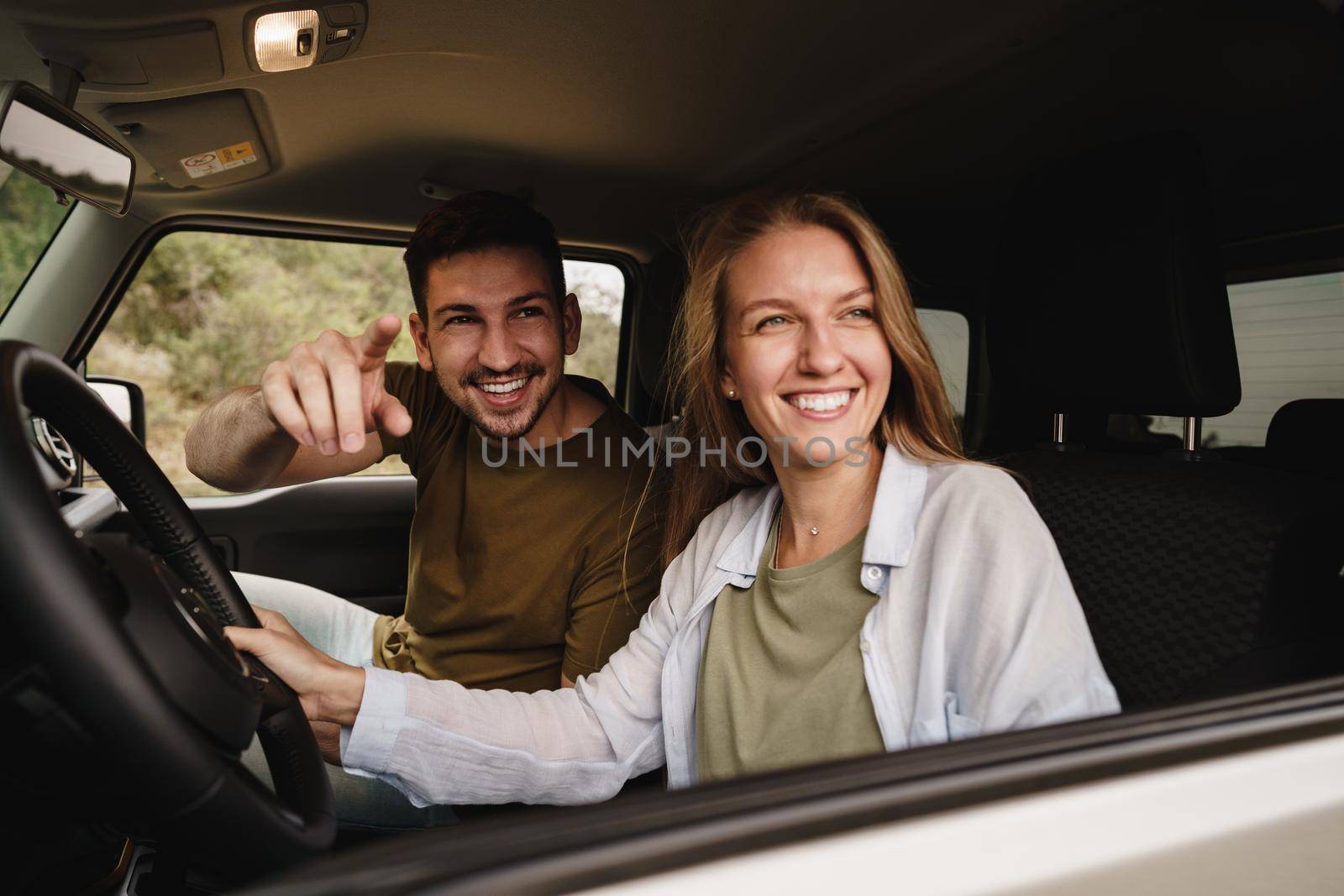 Beautiful young smiling couple sitting on front passenger seats and driving a car