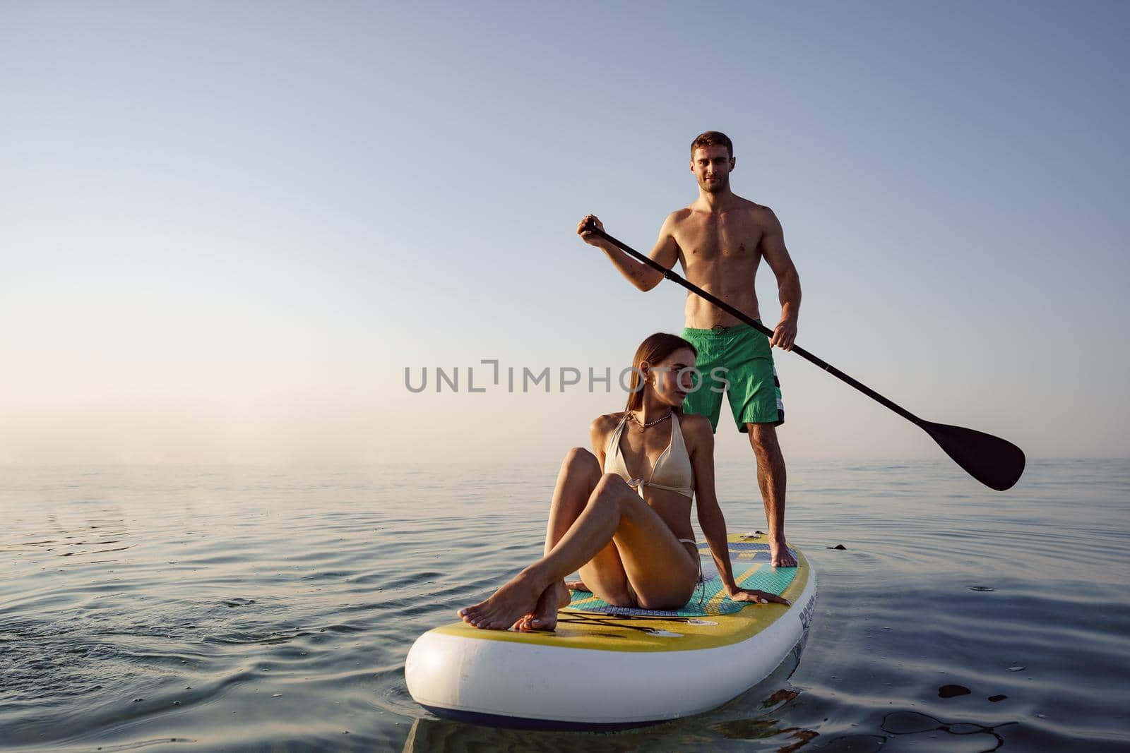 Couple of tourists young man and woman having fun paddleboarding at sea at sunset