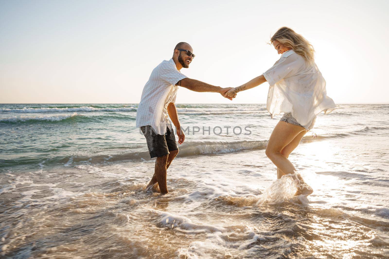 Young beautiful couple walking on beach near sea at sunset