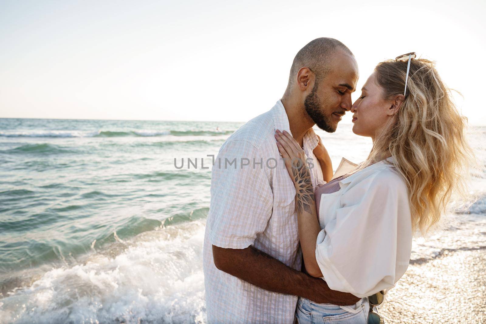 Beautiful young couple hugging on the beach by the water, close up