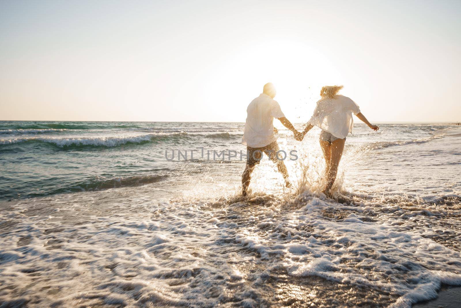 Young beautiful couple walking on beach near sea at sunset