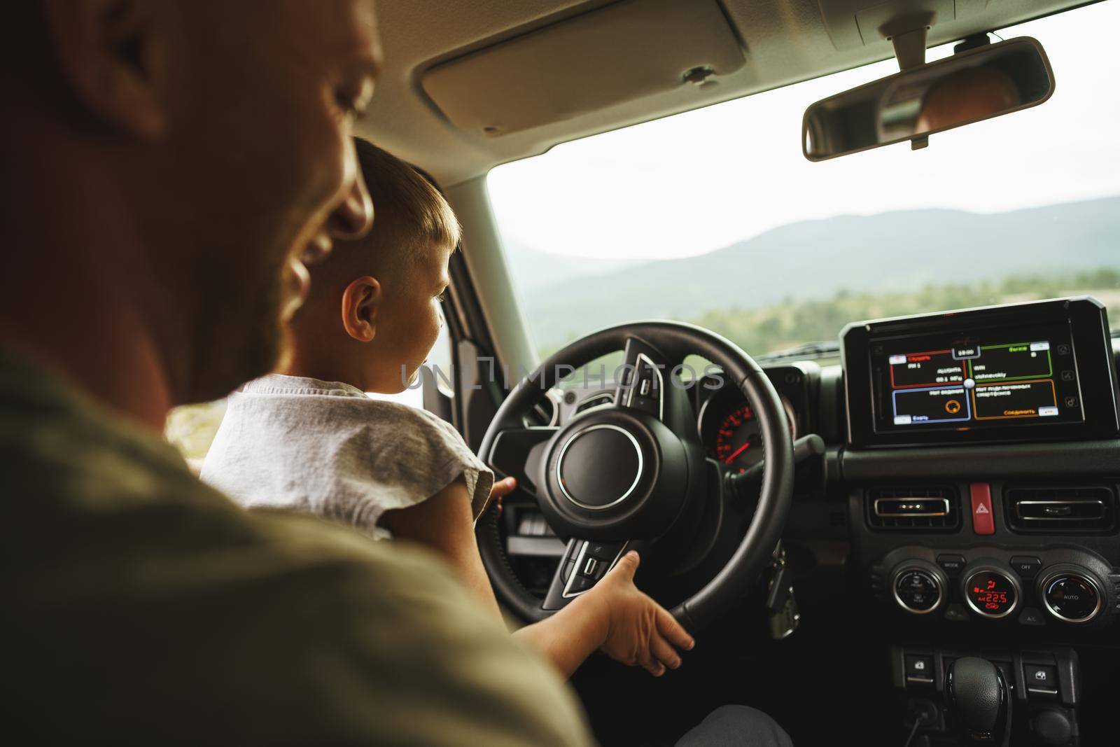 Father teaches little son to drive on road trip, close up