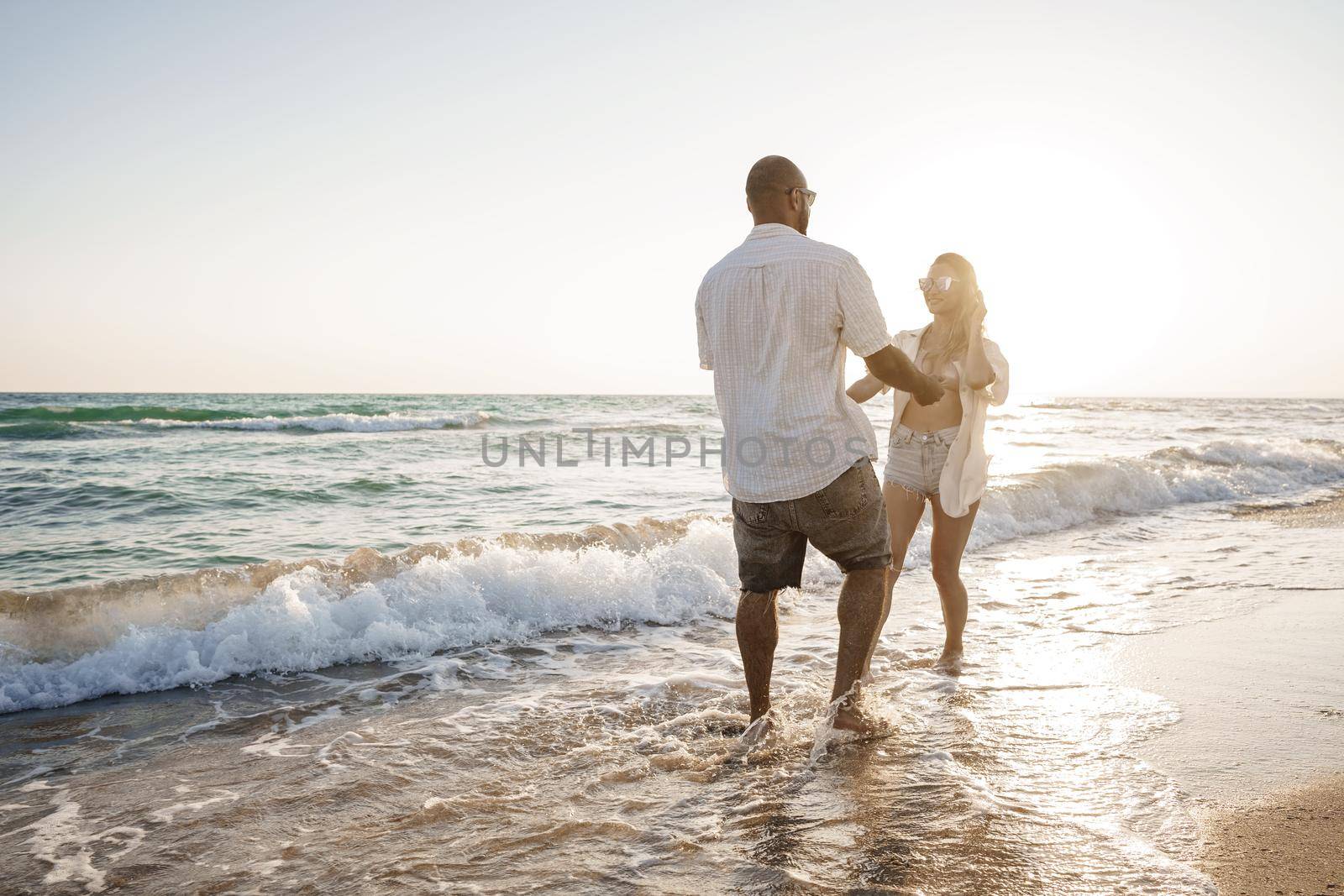 Young beautiful couple walking on beach near sea at sunset