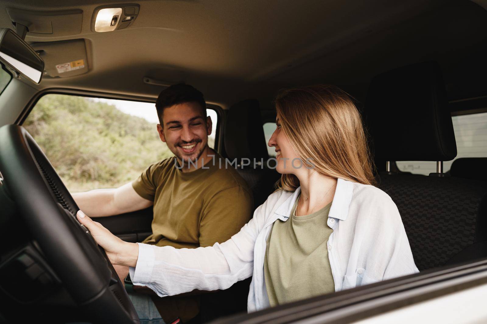 Beautiful young smiling couple sitting on front passenger seats and driving a car