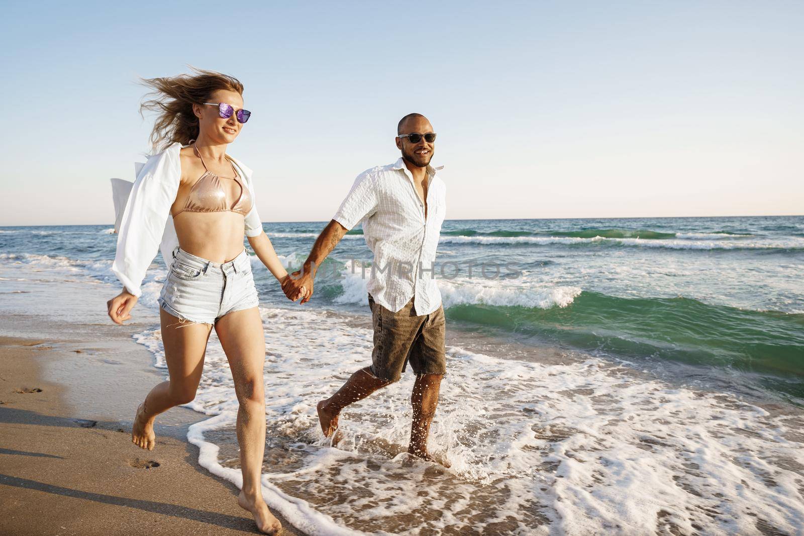 Young beautiful couple walking on beach near sea at sunset