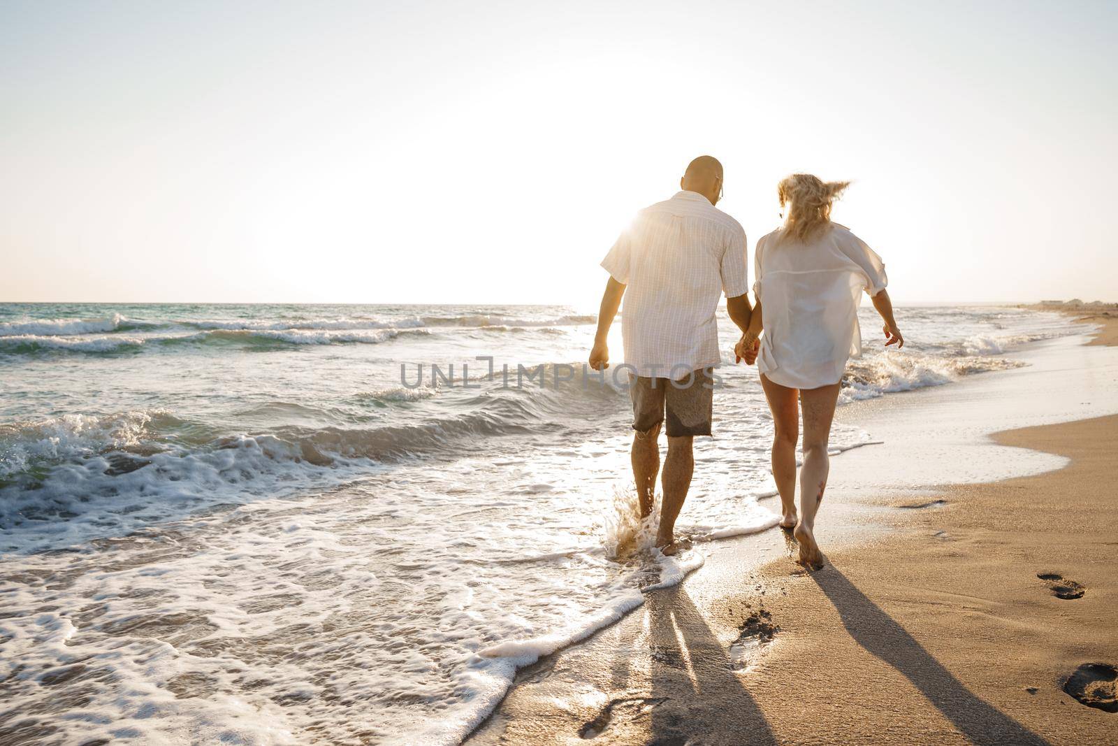 Young beautiful couple walking on beach near sea at sunset