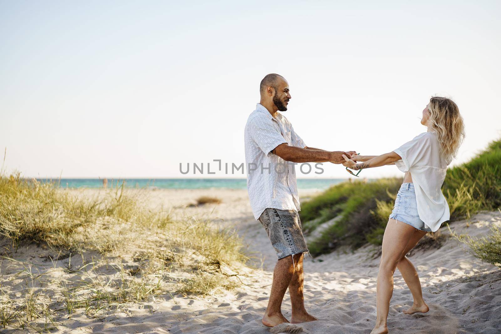 Young happy couple holding hands and walking together to the beach ocean on summer day